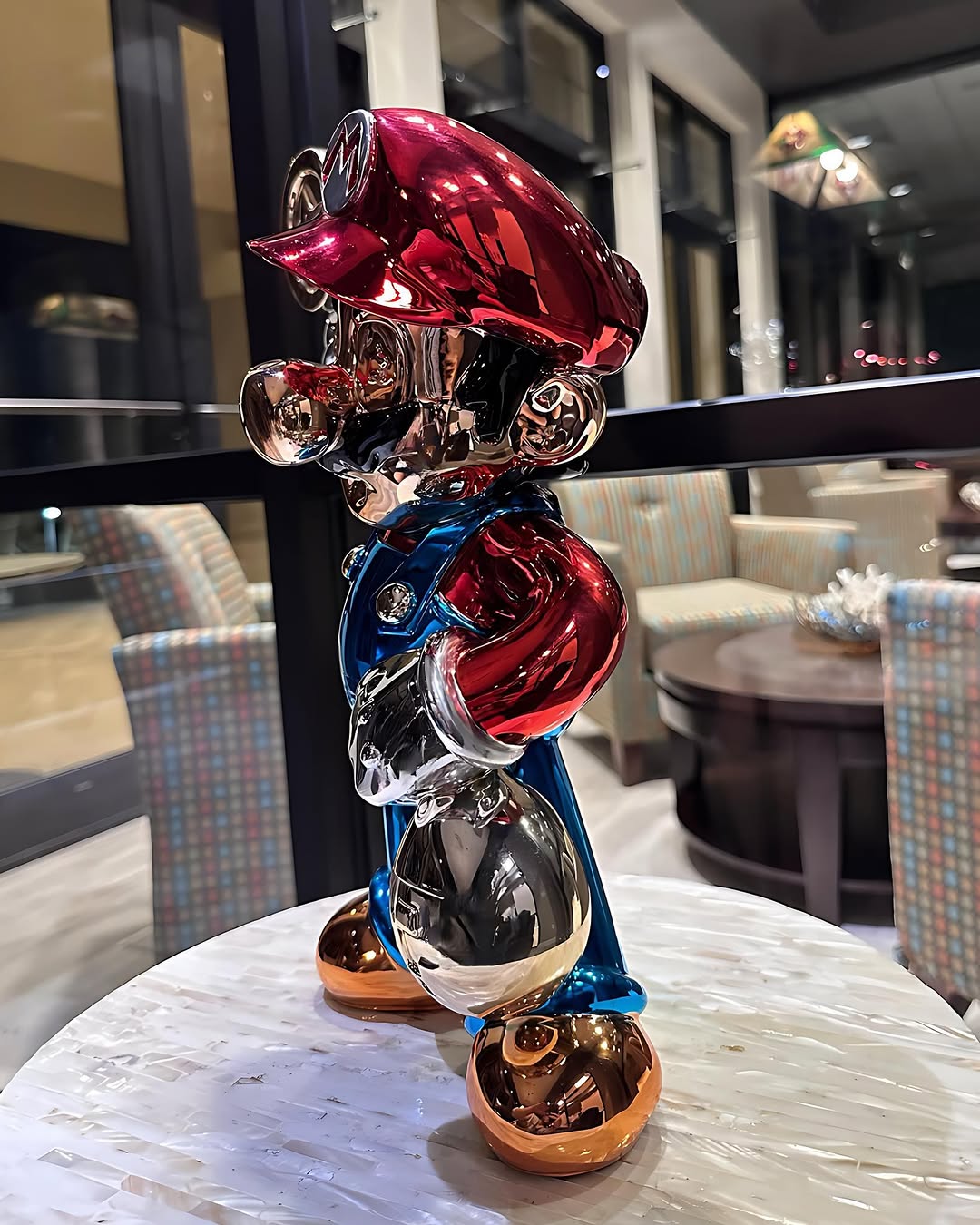 Side view of Super Mario chrome pop art statue with red, blue, and gold high-gloss finish on a table.
